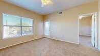 This single-story space is designed with a straightforward, functional layout visible across its several rooms. The living area is generously sized, finished with neutral beige carpet and painted in a warm cream tone that carries throughout the unit. A ceiling fan with integrated light fixture overhead provides both airflow and ambient lighting, while a large window and an exterior door with a glass panel allow abundant natural light and outdoor views. The open feel of this room is reinforced by clean, white baseboards and well-maintained walls.

The kitchen follows a galley-style configuration, featuring light wood cabinetry on both sides, light-toned laminate countertops, and wood-look plank flooring. White appliances — including a range, dishwasher, and refrigerator — are included. An electrical panel is accessible within the kitchen area.

The bedrooms mirror the living area's aesthetic, each carpeted, naturally lit by windows with outdoor views, and fitted with ceiling fans. The rooms offer a clean, neutral palette suited for a range of furnishing styles.

The bathroom is finished with wood-look flooring, a wood-tone vanity with overhead cabinetry, a white countertop, and a full-size bathtub, completing the unit's consistent and practical interior design.