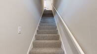 Located at 930 Terrapin Ln, Unit 204, this 2-bedroom, 2-bathroom residence spans 1,150 square feet across two floors. The ground floor hosts a private, automated single-car garage with a dedicated entry staircase leading up to the main living level. The expansive upper floor encompasses 1,070 square feet and features an open-concept kitchen and living room anchored by vaulted ceilings and light hardwood-style flooring. The kitchen is appointed with two-tone cabinetry — white upper cabinets and gray lower cabinets — complemented by white quartz countertops, stainless steel appliances, a matte black faucet, and an in-unit stacked washer and dryer. The living room opens to a private balcony through sliding glass doors, filling the space with natural light. Both bedrooms are carpeted and include ceiling fans, windows with blinds, and dedicated closets; the primary bedroom measures 190 square feet and features a spacious walk-in closet with wire shelving. The two bathrooms include hardwood-style flooring, gray vanities, and a sleek glass-enclosed shower with matte black fixtures. The unit's neutral color palette and clean architectural lines create a bright, modern ambiance throughout.