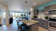 This well-designed single-floor unit offers a cohesive open-concept layout that seamlessly connects the kitchen, dining, and living areas. The kitchen is equipped with stainless steel appliances — including a refrigerator, range, microwave, and dishwasher — complemented by granite countertops, a subway tile backsplash, gray cabinetry, open shelving, and a peninsula island with bar seating. Wood-look flooring flows throughout the main living areas, adding warmth and continuity. The dining space sits adjacent to the kitchen island, while the living room features a teal accent wall, large windows, and sliding glass doors that open onto a private balcony with outdoor views of surrounding greenery, flooding the space with natural light. The bedroom is carpeted for comfort and features a teal accent wall, a walk-in closet, and a generously sized window with tree-lined views. The bathroom includes a combination tub and shower with white tile surround, a granite-topped vanity with dark cabinetry, and light tile flooring. Throughout the unit, a consistent teal and neutral color palette lends a modern, cohesive aesthetic.