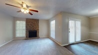 This single-story home is thoughtfully laid out across a well-connected floor plan, as illustrated by the 3D overview. The living room serves as the focal point of the home, anchored by a striking floor-to-ceiling natural stone fireplace that adds warmth and character. Plush carpeting, a ceiling fan with light fixture, a textured ceiling, and multiple windows with blinds complete the space. Glass panel doors lead to the exterior, filling the room with natural light. The living area flows into a separate dining space, distinguished by hardwood-style flooring and a pendant light overhead, alongside a built-in storage cabinet. The kitchen is equipped with warm oak cabinetry, light countertops, a double stainless steel sink, a dishwasher, and hardwood-style flooring, with a window above the sink providing natural light. The bedrooms are carpeted and feature ceiling fans, natural light from windows, and generous closet space—one bedroom notably offers dual closets. Both bathrooms include tub-shower combinations with textured tile surrounds, wooden vanity cabinetry, and hardwood-style flooring, delivering a consistent and functional aesthetic throughout the home.