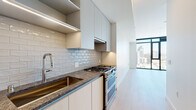 Located at 675 9th Ave in San Diego's Midtown neighborhood, this single-floor unit offers a contemporary design with clean lines and a bright, modern aesthetic. Light wood-tone flooring flows consistently throughout the space, complementing the white walls and creating a cohesive, airy feel.

The galley-style kitchen is well-appointed with flat-front cabinetry in a warm neutral tone, dark granite countertops, a subway tile backsplash, and stainless steel appliances including a gas range. Under-cabinet lighting adds both function and ambiance. The kitchen opens toward a spacious living area framed by floor-to-ceiling windows with bold black frames, offering sweeping views of the San Diego skyline and filling the space with abundant natural light.

The bedroom also benefits from large windows with city views, keeping the room bright and open. The bathroom features neutral tile flooring, a soaking tub with marble-style tile surround, a wall-mounted toilet, and direct access to a walk-in closet with built-in shelving. Near the entry, a conveniently tucked stacked washer and dryer unit provides in-unit laundry. The entryway features a smart lock for modern security.