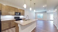 Located at 1000 Oak Street in Reynoldsburg, Ohio, this two-story home offers a well-designed layout with modern finishes throughout. The open-concept main level centers around a functional kitchen equipped with warm-toned cabinetry, black appliances including a refrigerator, range, and microwave, and a large island featuring a stainless steel sink and pendant lighting overhead. The kitchen flows seamlessly into the living area, which is bathed in natural light from a front-facing window. Hardwood-style flooring runs throughout the main level, adding warmth and continuity to the space. A half bathroom on the main floor features a granite-topped vanity and matching hardwood-style flooring. Upstairs, the bedrooms are carpeted for comfort and include windows that bring in natural light. A spacious walk-in closet with wire shelving provides generous storage. The upper-level full bathroom offers a wide double-sink vanity with granite countertops and wood cabinetry. An attached garage with an automatic opener provides convenient and secure parking. The home's neutral color palette and consistent finishes create a clean, cohesive aesthetic throughout both floors.
