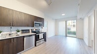 This thoughtfully designed 2-bedroom, 2-bathroom residence showcases a clean, modern aesthetic throughout its single-floor layout. Light wood-look flooring flows seamlessly across the main living areas, creating a cohesive and inviting atmosphere. The open-concept kitchen is a standout feature, equipped with a full suite of stainless steel appliances including a refrigerator, electric range, microwave, and dishwasher. Dark espresso cabinetry provides generous storage and contrasts elegantly with granite-style countertops and a classic white subway tile backsplash. Track lighting overhead adds a contemporary touch. The living area extends naturally from the kitchen and opens directly to a private balcony through sliding glass doors, allowing ample natural light to fill the space. Both bedrooms are bright and airy, each featuring large windows with outdoor views and light wood flooring. Three closets throughout the unit offer practical storage solutions. The two bathrooms are finished with large-format white tile flooring, dark wood vanities, granite countertops, and oversized mirrors. One bathroom includes a full soaking tub with tiled surround. The overall design is clean and neutral, providing a versatile canvas well-suited for a variety of living styles.