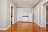 This studio is a thoughtfully arranged single-floor space that makes efficient use of every square foot. Throughout the unit, rich hardwood flooring in a warm honey tone provides a cohesive and inviting foundation. The main living area is generously sized relative to the overall footprint, offering flexibility for both sleeping and living arrangements. A ceiling fan with an integrated light fixture serves as the central overhead lighting source, contributing to comfortable airflow year-round. A window unit air conditioner is also present, providing additional climate control.

Built-in open shelving along one wall offers practical and attractive storage, while multiple closets provide additional organization options. The kitchenette is neatly tucked into one area and includes white cabinetry, a compact refrigerator, and a sink with counter space — all the essentials for everyday meal preparation.

The bathroom is a standout feature, finished with classic black-and-white mosaic tile work that climbs the walls and surrounds the full-sized soaking tub. A dark-finished vanity with a white basin adds contrast and character. Wood flooring continues into the bathroom, maintaining consistency throughout.

Neutral gray walls throughout the unit create a calm, versatile backdrop. The space benefits from natural light through its windows, enhancing the overall brightness and openness of this efficiently designed studio.
