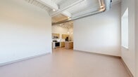 Located at 547 River St in Troy, NY, this modern one-bedroom, one-bathroom residence offers a thoughtfully designed single-floor layout with a distinct industrial-loft aesthetic. The open-concept living and kitchen area serves as the heart of the unit, showcasing soaring ceilings with exposed ductwork, painted wood plank ceiling details, and recessed lighting that create an airy, contemporary atmosphere. The kitchen features warm wood-tone cabinetry, a central island with a clean white countertop, sleek pendant lighting, and stainless steel appliances, making it both functional and stylish. Large windows in the living area allow natural light to filter in, offering views of the surrounding greenery. The bedroom is a well-proportioned, carpeted retreat with soft neutral tones and standard closet access. A dedicated den provides additional flexible space, ideal for a home office or study. The bathroom is finished with a wood-tone vanity, white countertop, and a large mirror. Additional conveniences include in-unit laundry, two closets, and connecting hallways that provide a logical flow throughout the unit. The overall palette of whites, warm wood tones, and neutral flooring contributes to a clean, modern, and welcoming ambiance.