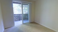 This single-floor residence offers a clean, functional layout with a welcoming and understated design. The main living area is finished with wall-to-wall carpeting in a neutral tone, providing a comfortable and quiet underfoot feel. Smooth, light-painted walls contribute to a calm and airy atmosphere throughout the space.

A prominent feature of the living area is the full-width sliding glass door, framed by vertical blinds, which floods the interior with generous natural light and offers direct access to a private outdoor balcony. The balcony is enclosed by horizontal slatted railing and is surrounded by mature trees, creating a tranquil, shaded outdoor retreat with a sense of privacy and a natural backdrop.

The overall ambiance of the space is quiet and neutral, offering a versatile canvas well-suited to a variety of interior styles. The connection between the interior living area and the outdoor balcony is a standout element, seamlessly blending indoor comfort with outdoor accessibility. Whether used as a relaxation area or an entertaining space, the balcony extends the functional living area and enhances the overall sense of openness within this single-floor residence.