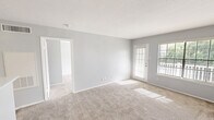 Located at 110 Lake Road in Lake Jackson, TX, this one-bedroom, one-bathroom unit offers a thoughtfully arranged single-floor layout with a clean, neutral aesthetic throughout. The combined kitchen and living room forms the heart of the unit, featuring light-colored carpet, soft gray walls, and white textured ceilings. Large windows fitted with horizontal blinds allow ample natural light to fill the space, while a patio door provides direct access to the private outdoor patio. The kitchen is defined by a breakfast bar-style peninsula with a light countertop, white cabinetry, a full suite of black appliances including a refrigerator, electric range, built-in microwave, and dishwasher, and durable wood-look flooring. A ceiling-mounted light fixture keeps the kitchen well-lit. The bedroom is a comfortable, carpeted room with a ceiling fan, a window with outdoor views, and access to a closet. The bathroom includes a full tub-shower combination with tiled surround, brushed nickel fixtures, a toilet, and wood-look flooring. A private patio rounds out the unit, offering outdoor space surrounded by mature trees.