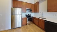 This single-floor residence presents a thoughtfully designed layout with clean finishes throughout. The kitchen serves as a functional centerpiece, outfitted with warm medium-toned wood cabinetry extending to the ceiling for generous storage. Stainless steel appliances — including a refrigerator, electric range, and built-in microwave — complement the light countertops, while a deep single-basin sink with a flexible gooseneck faucet and a black dishwasher complete the space. Light hardwood-style flooring runs through the kitchen and main living areas, adding warmth to the open feel.

The bedroom is finished with plush neutral carpet and features a window fitted with blinds that allows natural light to fill the room. A spacious walk-in closet adjacent to the bedroom offers wall-to-wall hanging rods and carpeted flooring, providing substantial storage capacity.

The bathroom includes a wood-toned vanity with a white countertop and an integrated sink, paired with a large mirror. Tile flooring ties the space together with a clean, polished look. The overall aesthetic throughout is neutral and bright, with white walls and consistent finishes creating a cohesive, move-in-ready environment.