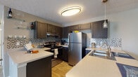 Located at 2800 John Steven Way in Reynoldsburg, Ohio, this single-floor residence offers a thoughtfully designed layout with a range of functional and stylish spaces throughout. The kitchen is a standout feature, showcasing dark espresso cabinetry, a mosaic tile backsplash, stainless steel appliances including a gas range and full-size refrigerator, light quartz countertops, and warm wood-look flooring — all illuminated by contemporary overhead lighting and a decorative pendant fixture. The open living room provides a comfortable gathering space with natural light streaming through window blinds, wood-look flooring, and a built-in electric fireplace media console as a focal point. The primary bedroom offers plush carpeting, neutral tones, and a walk-in closet, creating a calm and private retreat. A second bedroom features carpet flooring, a natural light window, and ample space. The full bathroom includes a dark vanity with a wide white countertop, wood-look flooring, built-in shelving, and a shower-tub combination. A dedicated laundry area with a full-size washer provides added in-unit convenience. Throughout the home, textured ceilings, neutral gray walls, and consistent finishes contribute to a cohesive and welcoming aesthetic.