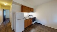 Located at 214 E Napoleon Rd in Bowling Green, Ohio, this single-floor unit offers a straightforward and functional layout designed for comfortable everyday living. The main living area features dark hardwood-style flooring, neutral cream-toned walls, and a window fitted with horizontal blinds that allows natural light to fill the space. A wall-mounted HVAC unit provides climate control, and the room offers ample space for furnishings. The kitchen is efficiently arranged with warm-toned wood cabinetry extending to the upper walls for generous storage, a double-basin sink with a dark countertop, a full-size refrigerator, and an electric range with an overhead ventilation hood. The flooring continues the dark hardwood-style finish seen throughout the main living area. The bedroom is carpeted in a neutral tone and features a window overlooking the outdoors, providing natural light and a view of surrounding greenery. A textured ceiling adds dimension to the room. The bathroom includes a wood-vanity cabinet with a white countertop and integrated sink, a mirrored medicine cabinet above, and a combination tub and shower enclosed with tiled walls. The overall ambiance of the unit is clean, practical, and well-maintained, making it a functional living space in Bowling Green.