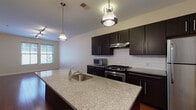Located at 750 Summer St in Stamford, Connecticut, this single-floor residence offers a thoughtfully designed layout with contemporary finishes throughout. The kitchen serves as a central highlight, featuring rich dark cabinetry, a classic white subway tile backsplash, granite countertops, and a large center island with a built-in sink illuminated by pendant lighting. Stainless steel appliances, including a gas range, refrigerator, and microwave, complete the modern culinary space. The kitchen flows seamlessly into the open living area, which is finished with warm hardwood flooring and track lighting, allowing for flexible furniture arrangements. Natural light enters through generously sized windows, creating a bright and welcoming atmosphere. The bedroom offers plush carpeting, dual windows with views of the surrounding neighborhood, and convenient access to both a walk-in closet and an adjacent bathroom. The bathroom is finished with dark slate tile flooring, a wall-mounted vanity with a large mirror, and a full tub and shower with white subway tile surround. A dedicated in-unit washer is tucked neatly near the entryway, adding practical convenience to this well-appointed Stamford residence.