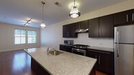 Located at 750 Summer St in Stamford, Connecticut, this single-floor residence offers a thoughtfully designed layout with contemporary finishes throughout. The kitchen serves as a central highlight, featuring rich dark cabinetry, a classic white subway tile backsplash, granite countertops, and a large center island with a built-in sink illuminated by pendant lighting. Stainless steel appliances, including a gas range, refrigerator, and microwave, complete the modern culinary space. The kitchen flows seamlessly into the open living area, which is finished with warm hardwood flooring and track lighting, allowing for flexible furniture arrangements. Natural light enters through generously sized windows, creating a bright and welcoming atmosphere. The bedroom offers plush carpeting, dual windows with views of the surrounding neighborhood, and convenient access to both a walk-in closet and an adjacent bathroom. The bathroom is finished with dark slate tile flooring, a wall-mounted vanity with a large mirror, and a full tub and shower with white subway tile surround. A dedicated in-unit washer is tucked neatly near the entryway, adding practical convenience to this well-appointed Stamford residence.