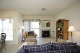 This single-floor residence offers a thoughtfully arranged layout that balances comfort and functionality. The open-plan living and dining area serves as the heart of the home, where soft carpet flooring, ceiling fans, and an abundance of natural light from sliding glass doors create a warm and inviting atmosphere. The living room features a tile-surround fireplace and direct access to an outdoor balcony, providing pleasant views of the surrounding landscape. Adjacent to the living area, a cozy dining nook accommodates a glass-top table and wrought iron chairs, positioned beside a window that fills the space with natural light. The kitchen is efficiently designed with white cabinetry, ample countertop space, and a pass-through opening that maintains a visual connection to the living and dining areas. The two bedrooms are generously sized, each appointed with plush carpeting, ceiling fans, and large windows that invite natural light. Both bedrooms include access to closet storage, offering practical organization. The two bathrooms are clean and functional, each featuring a vanity with under-sink storage, a tub-shower combination, and tile flooring. Throughout the home, a neutral color palette and consistent finishes contribute to a cohesive and comfortable living environment.