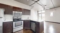 This urban loft-style residence offers a thoughtfully designed single-floor layout encompassing a bedroom, bathroom, kitchen, dining area, and hallway. The space is defined by its industrial aesthetic, highlighted by polished concrete floors that flow seamlessly throughout every room, exposed ceiling infrastructure with track lighting, and a crisp white color palette that enhances the sense of openness.

The kitchen is a standout feature, equipped with rich dark-toned cabinetry, a full suite of stainless steel appliances including a refrigerator, range, microwave, and dishwasher, and a peninsula with a white countertop that doubles as a dining or prep area. The open sightlines from the kitchen connect directly to the living and dining spaces, reinforcing the loft's communal feel.

The living area benefits from large sliding glass doors and clerestory windows that invite abundant natural light and offer views of the surrounding landscape, complemented by a ceiling fan and a wall-mounted mini-split system. The bedroom is a clean, minimalist space with its own window for natural light. The bathroom features a full soaking tub and shower combination with chrome fixtures and a floating vanity, maintaining the space's streamlined design.