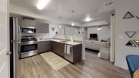 This single-floor residence is designed with a clean, contemporary aesthetic throughout. The open-concept kitchen anchors the main living area, outfitted with dark wood-grain cabinetry, stainless steel appliances, white quartz countertops, and pendant lighting above the peninsula. Wood-look flooring extends seamlessly from the kitchen into the adjacent living room, which features a tray ceiling detail and windows dressed with linen curtains, allowing natural light to filter in.

A dedicated dining area is positioned near a bank of windows, creating a bright, well-defined space finished with the same wood-look flooring. The layout includes multiple bedrooms, each carpeted for comfort. The primary bedroom is generously proportioned with windows providing natural light, while the additional bedrooms offer flexible configurations suitable for varied uses.

Two bathrooms serve the unit. The full bathroom features wood-look tile flooring, a dark vanity with white countertop, a large mirror, and a tub-shower combination. The secondary bathroom is a compact half-bath with a streamlined vanity and light flooring. Neutral gray walls are consistent throughout, contributing to a cohesive, modern ambiance across the entire space.