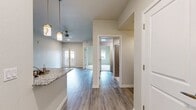 This 530-square-foot, one-bedroom, two-bathroom apartment at 2157 E Apache Blvd in Tempe, Arizona delivers a thoughtfully designed layout that maximizes every square foot. The open-concept living area features wood-look luxury vinyl plank flooring and neutral-toned walls, creating a clean, contemporary aesthetic throughout. French doors with glass panels invite natural light into the living space while providing outdoor access. The kitchen is well-appointed with two-tone cabinetry combining white upper cabinets and dark wood-grain lower cabinets, granite-style countertops, a tiled backsplash, and a full suite of stainless steel appliances including a refrigerator, range, microwave, and dishwasher. A peninsula with a sink adds prep space and separates the kitchen from the living area. The 130-square-foot primary bedroom features plush carpeting, a ceiling fan, a large window with outdoor views, and a double sliding closet. The bathrooms include wood-look vinyl flooring, and one features a tiled walk-in shower with modern fixtures. Throughout, recessed lighting and clean white trim contribute to the unit's bright, contemporary character.