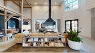 Located at 536 W Tremont Ave in Charlotte's vibrant Dilworth neighborhood, this expansive single-floor amenity space blends modern design with warm, residential character across a generously sized open-plan layout. Soaring double-height ceilings anchored by exposed light wood timber framing define the architectural identity of the space, while polished concrete floors flow seamlessly throughout, unifying the distinct zones within.

At the heart of the space, a dramatic suspended black metal fireplace serves as a bold focal point, surrounded by plush leather and upholstered sectional seating. Multiple lounge areas branch off from the central hub, each defined by deep navy accent walls, curated artwork, and a mix of textured furnishings that create intimate conversation nooks. A co-working area features a live-edge communal table beneath oversized pendant lighting, complemented by a coffee station and built-in cabinetry with wood paneling.

A bright dining area benefits from floor-to-ceiling steel-framed windows that flood the space with natural light and offer views of an outdoor pool. The full catering kitchen is outfitted with a long concrete-topped island, bar seating, subway tile backsplash, and stylish pendant fixtures. Throughout, lush greenery, layered textiles, and thoughtful lighting contribute to a sophisticated yet welcoming ambiance.