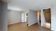 This three-story home offers a thoughtfully designed layout across multiple levels, providing ample space for comfortable living. The interior is finished in a clean, neutral color palette, with cool grey walls and white trim that create a bright, modern aesthetic throughout.

The main living area features durable hard-surface flooring in a warm brown tone, offering both practicality and visual warmth. A textured ceiling adds subtle dimension, while flush-mount lighting provides consistent illumination across the space. Visible HVAC venting integrated into the walls reflects a practical approach to climate control throughout the home.

The open flow of the main level connects seamlessly to adjoining rooms, with doorways leading to additional spaces that include what appears to be a utility or storage area. A staircase with white-painted railings provides access to the upper and lower levels, reinforcing the home's multi-floor design.

White interior doors are consistent throughout, contributing to the cohesive, clean finish of the space. The layout is well-suited for a variety of uses, offering flexible room configurations across all three floors. Overall, the space presents a move-in-ready environment with a neutral, versatile design that accommodates a range of furnishing styles and personal preferences.
