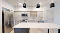 Located at 340 S 500 E in Salt Lake City, Utah, this contemporary one-bedroom, one-bathroom unit offers a well-designed open-concept floor plan with a clean, modern aesthetic throughout. Light-toned hardwood-style flooring runs continuously through every room, enhancing the bright and airy atmosphere created by recessed and pendant lighting.

The kitchen is a standout feature, outfitted with two-tone gray and white cabinetry, quartz countertops, stainless steel appliances including a range, built-in microwave, dishwasher, and refrigerator, as well as an open shelf for additional storage. A striking kitchen island with a white quartz top and bold navy blue base provides extra prep space and serves as a natural focal point.

The living room is generously proportioned and filled with natural light, featuring glass French doors that open to a private balcony with views of the surrounding Salt Lake City skyline and mountains. The bedroom offers a comfortable footprint with a window that brings in natural light. The bathroom is finished with light cabinetry, a quartz vanity, a backlit mirror, and a glass-enclosed shower, maintaining the unit's cohesive modern design throughout.