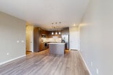 Located at 17607 East 61st Avenue in Denver, CO, this well-appointed 2-bedroom, 2-bathroom residence offers a thoughtfully designed single-floor layout. The open-concept living, dining, and kitchen area forms the heart of the home, featuring warm wood-toned cabinetry, quartz countertops, a central island with pendant lighting, and a full suite of stainless steel appliances including a range, microwave, and refrigerator. A textured tile backsplash and luxury vinyl plank flooring add modern detail throughout the main living space, which extends to a private balcony with outdoor views. The two bedrooms are carpeted for comfort; the primary bedroom offers a generous footprint with a ceiling fan and abundant natural light through multiple windows. Three closets, including a walk-in fitted with wire shelving systems, provide ample storage. The bathrooms are finished with wood-grain vanities, quartz counters, tile flooring, and a tub-shower combination. Additional conveniences include a dedicated laundry area, a pantry, a utility room, and a hallway connecting all spaces. Neutral taupe wall tones and clean white trim create a cohesive, move-in-ready aesthetic throughout.