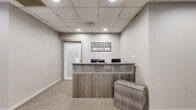 Windsor Club is a generously sized fitness and wellness facility occupying a single floor and offering a comprehensive range of amenities designed to support an active lifestyle. The space is introduced by a polished reception area, where a modern wood-paneled front desk sits beneath a drop-panel ceiling with recessed lighting, setting a clean, professional tone throughout.

The fitness floor is divided into distinct functional zones. A large cardio area is lined with an extensive array of treadmills, ellipticals, stationary bikes, and other machines, bathed in natural light from expansive windows that frame city skyline views. Adjacent to this is a strength training zone featuring Cybex cable machines, free weights, weight benches, and a full dumbbell rack, all set on durable rubberized flooring with floor-to-ceiling mirrors that amplify the sense of space.

A dedicated studio room provides an open, carpeted area with mirrored walls and windows with urban views, equipped with kettlebells, stability balls, yoga mats, and other group fitness accessories — ideal for classes or personal training sessions. Transitional corridors feature glass partitions and additional mirrors, maintaining an open and connected feel throughout. The overall design is neutral and contemporary, with light grey tones, drop ceilings, and abundant natural light creating a bright, functional environment.