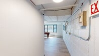 This expansive single-floor space masterfully blends industrial character with modern design, offering a generously sized open floor plan bathed in natural light from large black-framed windows throughout. The exposed white-painted concrete block walls and visible overhead ductwork and piping celebrate the building's industrial heritage, while wide-plank light oak hardwood flooring and contemporary furnishings create a warm, inviting atmosphere.

At the heart of the space is a stunning full kitchen featuring stainless steel appliances including double wall ovens, a refrigerator, and a dishwasher, all complemented by a dramatic waterfall-edge marble island with seating for several guests. Bold teal-painted accent walls add vibrant pops of color and visually define distinct zones within the open layout.

The lounge area is anchored by a plush sectional sofa, a sculptural round coffee table, and a woven pendant light, while corner windows frame impressive city views. A casual dining nook with a round table and woven rattan chairs offers an intimate setting. A textured teal feature wall creates a cozy banquette seating area ideal for small gatherings. Toward the back, a game room with a pool table and additional windows rounds out the space, making it a highly versatile and well-appointed destination for both social and recreational use.