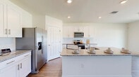 Located on Peaceful Brook Loop in Punta Gorda, Florida, this two-story home offers a well-organized layout spread across two floors, with the upper level providing the larger share of living space. The main floor features an open-concept kitchen and living area connected by wood-look plank flooring that flows consistently throughout the home. The kitchen is appointed with crisp white shaker cabinetry, granite countertops, stainless steel appliances including a refrigerator with ice maker, electric range, and microwave, plus a central island with a sink — ideal for both cooking and casual dining. An elegant arched doorway connects the hallway to the living area, adding architectural character to the otherwise clean, modern interior.

The upper floor houses the generously sized primary bedroom, which features abundant natural light through large windows with outdoor views. The primary bathroom includes a dual-sink vanity with granite countertops and white cabinetry. A walk-in closet with wire shelving provides substantial storage. The four additional bedrooms are bright and well-proportioned, each with wood-look flooring and natural light. A dedicated laundry room with a full-size washer and dryer adds practical convenience. The home's neutral color palette and consistent finishes create a cohesive, move-in ready atmosphere throughout.