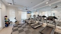 Located at 2211 Parklake Dr NE in Atlanta, Georgia, this well-appointed fitness center offers a bright and modern environment designed to support a full range of workout routines. The space is laid out on a single floor and features a clean, contemporary aesthetic with crisp white walls, recessed lighting, and ceiling fans that ensure comfortable air circulation throughout.

The main exercise area is outfitted with a robust selection of cardio equipment, including treadmills, elliptical trainers, and a recumbent bike, catering to a variety of fitness preferences. Floor-to-ceiling mirrors line one wall, visually expanding the space and allowing users to monitor their form during workouts. A dedicated section of the floor is finished with a checkered carpet tile pattern, providing cushioning underfoot for high-impact activities, while smooth hardwood-style flooring borders the perimeter for a polished finish.

Natural light flows in generously through large windows fitted with roller shades, creating an inviting and energizing atmosphere. A mounted flat-screen television is positioned for easy viewing from the cardio equipment. Additional fitness accessories, including a rack of medicine balls, are available to support strength and cross-training exercises. Large glass panel doors connect the fitness center to adjacent areas, enhancing the open and airy feel of the overall space.