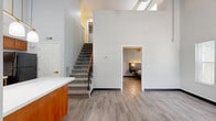 Located at 2084 S Hamilton Rd in Columbus, Ohio, this two-story residence offers two bedrooms and three bathrooms across a thoughtfully laid-out floor plan. The main floor serves as the heart of the home, encompassing the living room, a combined kitchen and dining area, and one of the bedrooms. The kitchen is well-appointed with warm wood cabinetry, a white countertop peninsula, black appliances including a refrigerator, electric range, microwave, and dishwasher, and pendant lighting above the counter—creating a functional yet inviting space. Durable wood-look flooring runs throughout the main level, complementing the clean white walls. A carpeted staircase with a wood handrail connects the main floor to the upper level, which houses an additional bedroom. The spacious primary bedroom features a built-in headboard wall with integrated sconce lighting and floating nightstands, angled ceilings, and track lighting. The second bedroom includes built-in shelving and a window for natural light. Three bathrooms are distributed across both floors, each featuring tub/shower combinations with grab bars, and at least one includes a granite-topped vanity with wood cabinetry. A utility room and three closets provide ample storage throughout the home.