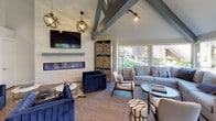 Located at 444-445 N Amelia Ave in San Dimas, California, this single-story community space delivers a thoughtfully curated blend of rustic and contemporary design. The architecture is defined by soaring vaulted ceilings with exposed painted beams, wood-look flooring throughout, and an abundance of natural light streaming in through large windows that frame views of mature surrounding greenery.

The welcoming entry foyer features striking sculptural art pieces, including a large metalwork horse sculpture, which establishes the space's artistic character. Painted exposed beam trusses add architectural drama overhead. A glass-enclosed fitness center is visible from the main corridor, lined with reclaimed wood accent walls and equipped with exercise equipment, providing both functionality and visual interest.

The lounge area is a standout, anchored by a sleek linear fireplace set against a stone tile wall, flanked by built-in firewood storage. Vaulted ceilings, globe pendant lighting, and a cozy sectional arrangement with garden views create an inviting atmosphere. A separate dining nook features a kitchenette with tile backsplash. Throughout the space, reclaimed wood accent walls, curated artwork, and cohesive navy and neutral tones reinforce a warm, modern-rustic ambiance.