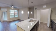 This single-story, 2-bedroom, 2-bathroom residence offers a well-designed open-concept layout. The kitchen serves as a central feature, showcasing dark espresso cabinetry, granite-style countertops, and a spacious island with a double-basin sink illuminated by three pendant lights. Black appliances, including a gas range, microwave, and refrigerator, complement the subway tile backsplash. Track lighting and pendant fixtures provide layered illumination throughout.

The open living area extends from the kitchen, featuring wood-style plank flooring and a ceiling fan. Natural light enters through blinded windows with exterior views. An in-unit laundry area with overhead wire shelving adds everyday convenience.

Both bedrooms include ceiling fans, wood-style flooring, and closet access. The primary bedroom connects directly to a bathroom featuring a dual-sink vanity with granite-style countertops, dark cabinetry, a large mirror, and a walk-in closet. The second bathroom offers a white tiled tub-shower combination with chrome fixtures. Neutral tones and consistent finishes throughout create a cohesive, modern ambiance.