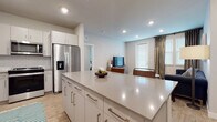 This single-floor residence showcases a thoughtfully designed open-concept layout that seamlessly connects the kitchen and living spaces. The kitchen is well-appointed with white shaker-style cabinetry extending to the ceiling, a subway tile backsplash, stainless steel appliances including a French door refrigerator with ice dispenser, a gas range, built-in microwave, and dishwasher. A generously sized central island with a light quartz countertop provides additional prep space and casual seating.

The open living area flows naturally from the kitchen and features light wood-style flooring, recessed lighting, and access to an exterior door framed by large windows fitted with blinds and decorative drape panels. The bedrooms are carpeted and bathed in soft, neutral tones, with windows that invite natural light. Each room offers comfortable proportions suitable for full-sized furniture.

The bathrooms include a full bath with a tub-shower combo, quartz vanity countertops, white cabinetry with brushed nickel hardware, and wood-style flooring. A secondary bathroom features a stand-alone walk-in shower with white tile surround and a glass sliding door. The overall aesthetic is clean and contemporary, with a consistent palette of whites, grays, and soft blues throughout.