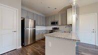 Located at 5056 Westerville Rd in Columbus, Ohio, this 2-bedroom, 1-bathroom unit is thoughtfully designed to maximize functionality within a compact, single-floor layout. The open-concept kitchen and living area serves as the heart of the unit, where the kitchen stands out with gray shaker-style cabinetry extending to the ceiling, a classic white subway tile backsplash, granite countertops, and a full suite of stainless steel appliances including a refrigerator, range, microwave, and dishwasher. A peninsula with a undermount sink and pendant lighting above provides additional prep space and separates the kitchen from the living area. Wood-style plank flooring runs throughout the kitchen and living spaces, adding warmth and visual continuity.

The living area is bright and open, featuring a glass exterior door flanked by a window that allows natural light to flow in and provides outdoor access. Both bedrooms are carpeted for comfort, each featuring neutral-toned walls, a window with blinds, and adequate space for standard furnishings. The primary bedroom offers a generously sized footprint relative to the overall layout. The bathroom features wood-style flooring, a granite-topped vanity with gray cabinetry, and clean, neutral wall tones consistent with the rest of the unit.