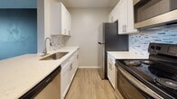 This 2-bedroom, 1-bathroom residence is contained on a single floor and offers a well-organized layout designed for comfortable, functional living. The open living area features durable wood-style flooring in a warm gray tone, neutral-painted walls, and a tiled ceiling, creating a clean and cohesive aesthetic. A large window allows natural light to flow in and provides views of the surrounding greenery, enhancing the sense of openness.

The kitchen is designed in a galley style, maximizing efficiency with white shaker cabinetry, light quartz countertops, a mosaic tile backsplash, and stainless steel appliances including a refrigerator, range, dishwasher, and microwave. A pass-through peninsula connects the kitchen to the living area, making it ideal for everyday use. Light hardwood-style flooring continues through this space.

Both bedrooms carry the same wood-style flooring and neutral tones, with windows that invite natural light and outdoor views. Each room offers a calm, versatile environment suitable for a variety of furniture arrangements.

The bathroom is clean and functional, featuring a full tub-shower combination with white subway tile surround, wood-style flooring, and classic white fixtures. The overall design of the unit emphasizes practicality and modern simplicity throughout.