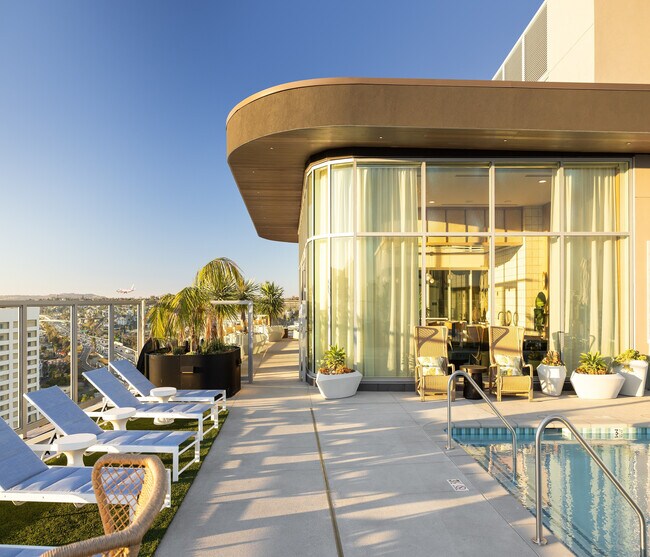 Lujosa área de piscina en la azotea con elegantes sillones, vistas panorámicas de la ciudad y un moderno salón con revestimiento de vidrio en un entorno vibrante de gran altura. - Ancora Apartments