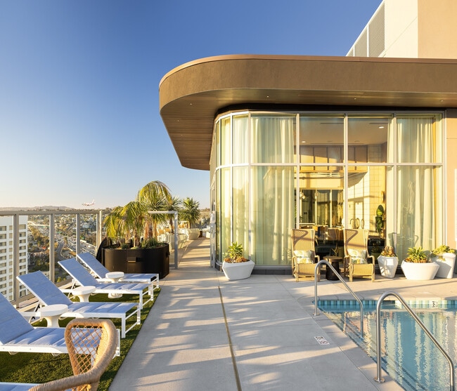 Luxurious rooftop pool area with sleek lounge chairs, panoramic city views, and modern glass-encased lounge in a vibrant high-rise setting. - Ancora Apartments