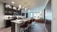 Located at 791 Morris Avenue in Ashwaubenon, Wisconsin, this single-floor residence showcases a thoughtfully designed open-concept layout with modern finishes throughout. The kitchen serves as a central highlight, featuring dark espresso cabinetry, stainless steel appliances including a French door refrigerator, electric range, and built-in microwave. A large white quartz island anchors the space, offering an integrated sink, built-in wine rack, and seating for multiple guests beneath elegant pendant lighting. A subway tile backsplash adds a clean, contemporary touch.

The kitchen transitions seamlessly into the living area, where large windows allow generous natural light to filter in. The living room includes built-in glass corner shelving and ample space for varied furniture arrangements. Wood-look plank flooring runs throughout the main living areas, while plush carpet provides comfort in the bedroom.

The bedroom is a calm retreat, benefiting from multiple windows with roller shades, warm-toned wood furnishings, and access to a walk-in closet. The bathroom features dark cabinetry with chrome hardware and light-toned flooring. An additional flexible room offers space suitable for a den or guest room. The overall aesthetic is cohesive, contemporary, and well-appointed.