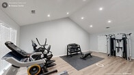 Located at 1719 Palmer St in Durham, NC, this purpose-built exercise room offers a well-appointed private fitness space designed for comprehensive workouts. The room is characterized by striking vaulted ceilings that rise to a dramatic peak, lending an open, airy feel that enhances the sense of space. Recessed lighting is installed throughout, providing bright, even illumination across the entire floor area.

The flooring consists of light-toned luxury vinyl plank, offering both durability and a clean, modern aesthetic. A protective rubber mat defines the strength training zone, keeping the workout area organized and functional.

The cardio section is equipped with a treadmill, elliptical trainer, and stationary bike, all positioned near a large window fitted with white blinds that admits natural light. The strength training area features a multi-functional cable machine, a dumbbell rack with a full set of weights, and an adjustable workout bench, supporting a wide range of resistance exercises.

Access is provided through an interior door as well as a glass-panel exterior door, allowing for ventilation and easy entry. The walls are finished in a neutral light gray, complementing the modern, minimalist design. A potted plant adds a touch of greenery, completing this clean and fully functional private fitness environment.