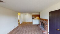 This single-floor residence offers a functional and straightforward layout designed for comfortable everyday living. The main living area is generously sized, featuring wall-to-wall carpeting, a textured ceiling, and a ceiling fan for year-round comfort. A standout feature of the living room is the full-height brick fireplace with a raised hearth, serving as a classic focal point. Natural light enters through a window along one wall, and the space flows openly toward the kitchen area.

The kitchen follows a galley-style configuration, lined on both sides with warm wood-toned cabinetry that provides ample storage. It is equipped with a coil-burner range, a refrigerator, a microwave, and a single-basin sink with adjacent counter space. The light-toned tile flooring and a back door add practicality to the space.

Two carpeted bedrooms offer comfortable retreats, each with windows that bring in natural light and sufficient space for standard furnishings. The bathroom is cleanly appointed with a single-sink vanity featuring wood cabinetry, a wall-mounted light fixture above the mirror, and a full tub-shower combination with tile surround and light flooring throughout. The overall layout is practical and well-organized across its single level.