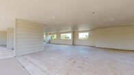 Located at 600 E Marble St in Wylie, TX, this generously sized single-floor space offers a versatile and open layout ideal for a range of uses. The interior is defined by its clean, neutral palette, with white horizontal shiplap-style wall paneling and light-toned large-format tile flooring that runs throughout, lending a bright and cohesive aesthetic.

The expansive main living area benefits from an abundance of natural light, delivered through multiple oversized windows positioned along the walls. These windows frame views of the surrounding mature tree canopy, creating a pleasant connection to the outdoors. The smooth, flat ceilings with recessed lighting contribute to the airy, uncluttered feel of the interior.

Structural columns punctuate the open floor plan, providing architectural definition without compromising the sense of spaciousness. A standout feature of the space is the expansive covered outdoor terrace, accessible from the main interior and enclosed by sleek black wrought iron railings. This open-air area is equally generous in scale, offering panoramic views of the surrounding greenery and neighborhood, making it well-suited for gatherings or events.

A brick accent column adds a contrasting textural detail to the terrace area, complementing the predominantly white interior finishes. The combination of the bright interior, seamless indoor-outdoor flow, and substantial square footage makes this a highly adaptable and visually appealing space.