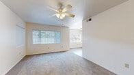 This single-story, 3-bedroom, 2-bathroom home offers a practical and comfortable layout designed for everyday living. The living area features plush carpeting, large windows with vertical blinds that invite natural light, and a ceiling fan with a light fixture, creating a bright and airy atmosphere. Sliding glass doors in the living space lead to an outdoor patio area, extending the sense of openness. The kitchen is efficiently designed with light wood cabinetry, white appliances including a range, refrigerator, and dishwasher, white countertops, and wood-style flooring that continues into the hallway. A peninsula counter provides a convenient pass-through connection to the adjacent living area. The hallway connects the main living spaces to the bedrooms and bathrooms, featuring the same warm wood-style flooring for a cohesive flow. Each of the three bedrooms is carpeted and equipped with ceiling fans, providing comfort throughout. The spacious primary bedroom offers generous room dimensions. Both bathrooms are clean and functional, with one featuring a tub-shower combination with tile surround, wood-style flooring, a large vanity mirror, and ample countertop space. The overall ambiance of the home is neutral, bright, and move-in ready.