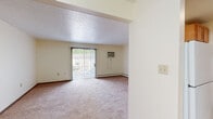 Located at 1100 E Liberty St in Girard, Ohio, this single-floor unit offers a straightforward, functional layout with a neutral color palette throughout. The living area is generously proportioned, featuring wall-to-wall carpet, a wall-mounted air conditioning unit, and a baseboard heating system. A sliding glass door with vertical blinds opens to an outdoor view, allowing natural light to fill the room and creating a pleasant, open ambiance.

The kitchen is efficiently designed with warm-toned wood cabinetry providing ample storage above and below. A double stainless steel sink sits atop light granite-style countertops, complemented by a dishwasher and full-size white refrigerator and range. The kitchen flows openly toward the living space via a partial dividing wall, maintaining a connected feel.

The bedrooms are carpeted and well-sized, each featuring closet storage—one with a spacious walk-in closet with a full-length hanging rod, and another with a sliding-door closet. A window in the bedroom allows for natural light and outdoor views.

The bathroom includes a full tub-shower combination, vanity with medicine cabinet mirror, and tile-style flooring, maintaining a clean and practical aesthetic consistent with the rest of the unit.