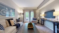 This well-appointed three-bedroom, two-bathroom residence in Columbus, Ohio offers a thoughtfully designed single-floor layout that maximizes comfort and functionality. The living room serves as the heart of the home, featuring neutral-toned walls, plush carpeting, and a set of French doors that open to a private balcony with lush outdoor views, filling the space with natural light. The galley-style kitchen is equipped with warm wood cabinetry, granite-look countertops, black appliances including a range, refrigerator, and dishwasher, and durable hardwood-style flooring. Adjacent to the kitchen, the dining area provides an intimate space for meals, illuminated by a pendant light overhead. The primary bedroom offers a comfortable retreat with plush carpet, a natural light-filled window, and generous closet space. The two additional bedrooms are similarly carpeted and feature closets, making them ideal for guests or a home office. Both bathrooms are finished with tile flooring, warm wood vanities, and well-lit mirrors. One bathroom features a walk-in shower, while the other includes a soaking tub-shower combination. A connecting hallway ties all rooms together in a cohesive, easy-to-navigate layout throughout this inviting home.