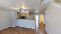 This two-bedroom, two-bathroom two-story home in Kansas City, Missouri offers a well-designed layout spread across two floors. The main level features an open-concept living and kitchen area with warm hardwood-style flooring throughout. The kitchen is equipped with stainless steel appliances—including a refrigerator, range, and microwave—complemented by light wood cabinetry, a peninsula counter, and a track lighting system. The adjacent living area benefits from natural light through a large window and provides a welcoming, open feel, with a staircase leading to the upper level. A full bathroom with a tub/shower combo is also found on the main floor. Upstairs, the spacious primary bedroom impresses with vaulted ceilings, a ceiling fan, a charming arched window, soft carpet flooring, and direct access to a walk-in closet and a private en-suite bathroom featuring a glass-enclosed shower. The second bedroom also features vaulted ceilings, a ceiling fan, light hardwood-style flooring, and a door leading to an outdoor balcony area with exterior views. Neutral tones and clean finishes are carried throughout, creating a cohesive and move-in-ready aesthetic across the entire home.