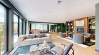 Located at 1105 Pleasant St in Oak Park, IL, this single-floor community lounge space offers a thoughtfully designed, open-plan layout that accommodates a variety of social and relaxation needs. The interior is defined by a cohesive modern aesthetic, anchored by rich forest-green accent walls that contrast beautifully with light-toned hardwood flooring running throughout.

The main living area is generously proportioned, featuring a plush sectional sofa arranged around a striking marble-topped coffee table atop a deep teal area rug. Floor-to-ceiling windows along the perimeter flood the space with natural light and provide open views of the surrounding Oak Park streetscape, with sheer white curtains softening the light when desired.

Multiple distinct seating zones encourage both conversation and quiet retreat. Swivel lounge chairs in muted blue tones, a leather lounge chair, and mid-century inspired accent chairs are thoughtfully positioned across the floor. A built-in wood shelving unit displays curated décor, books, and greenery, lending warmth and character to the space.

A separate nook near the elevator corridor features bold green walls, colorful wall art, and intimate seating. Adjacent to the main area, a dining zone with rattan-back chairs is visible through glass partitions. A beverage station with cabinetry completes the amenity offerings, making this space both functional and inviting.