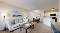 Located at 1121 Nine Iron Dr in Green, Ohio, this single-floor residence offers a thoughtfully designed layout with a warm, neutral color palette throughout. The open-concept living and dining area is bright and inviting, featuring plush carpeting, soft natural light from large windows dressed with sheer curtains, and a seamless flow between spaces. The living area provides ample room for comfortable furnishings, while the adjacent dining space connects naturally to the kitchen via a peninsula-style breakfast bar.

The kitchen is equipped with white cabinetry, light countertops, and a full suite of black appliances including a range, over-the-range microwave, and refrigerator. Wood-look flooring adds a clean, practical finish to this functional cooking space.

Two well-sized bedrooms each feature plush carpeting and windows that allow natural light to filter in through sheer panels, creating a calm and restful atmosphere. Both rooms offer comfortable proportions suitable for standard bedroom furnishings.

The residence includes two bathrooms, each finished with wood-look flooring, light countertops, and clean white fixtures. One bathroom features a vanity with mirror and a shower-tub combination, while the second offers a similarly clean and functional design. Overall, the space presents a cohesive, comfortable living environment ideal for everyday living.