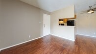 Located at 110 E Hawkins Pkwy in Longview, TX, this single-story unit offers a practical and efficiently designed layout with one bedroom, two bathrooms, and two closets. The open-concept living and dining area features warm hardwood-style flooring and neutral beige walls, creating a clean and cohesive aesthetic throughout. A textured ceiling adds classic character to the shared living space. A sliding glass door fitted with vertical blinds allows natural light into the living area while providing easy access to the outdoors. The kitchen is positioned adjacent to the living and dining area and features a pass-through window with upper cabinetry in warm wood tones, a built-in range hood, and a refrigerator. The bedroom is carpeted for comfort, features a window with blinds that admits natural light, and provides direct access to a closet and the adjoining areas. Two bathrooms serve the unit, one of which includes a full bathtub and shower combination with white subway tile surround and chrome fixtures. Throughout the unit, consistent neutral tones, textured ceilings, and clean white trim create a simple and functional living environment well-suited for everyday living.