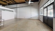 Located at 1702 Fairview St in Greensboro, NC, this industrial-style loft blends raw architectural character with functional modern living across a single, generously sized floor. The open main living area immediately impresses with soaring ceilings, exposed white-painted brick walls, and a striking wood-paneled ceiling with visible structural beams and ductwork. Polished concrete floors run throughout the entire space, reinforcing the industrial aesthetic. Large multi-pane industrial windows along the front facade flood the interior with natural light, while ceiling fans provide comfort throughout.

The well-appointed kitchen features dark wood cabinetry, black appliances including a range and full-size refrigerator, a stainless steel prep island, and pendant lighting hung dramatically from the tall ceiling above. The spacious primary bedroom offers a ceiling fan and direct access to the private areas of the unit. Two walk-in closets provide ample storage, each equipped with wire shelving systems. The clean, minimalist bathroom includes grab bars, a vanity, and neutral finishes. The thoughtful layout balances open, loft-style living with clearly defined private spaces, making this a versatile and distinctive urban residence.