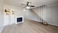 Located in Spring, TX, this two-story home offers a well-organized layout spread across two floors. The main level features two living areas with light wood-look flooring, crown molding, and ceiling fans throughout. A cozy fireplace anchors the main living room, complemented by built-in shelving — perfect for display or storage. The open staircase with white balusters and carpeted treads connects both levels with a clean, modern aesthetic. The kitchen is efficiently designed with white cabinetry, quartz-style countertops, subway tile backsplash, and black appliances, alongside a convenient pantry for added storage. Upstairs, the spacious primary bedroom features vaulted ceilings, plush carpet, and a generous walk-in closet with wire shelving. A second bedroom on the upper level offers hardwood-look flooring, a ceiling fan, and a large window that brings in natural light. The full bathroom includes a white vanity with a quartz countertop, a tiled shower/tub combination, and a clean, neutral finish throughout. Three closets across the home provide ample storage. The upper landing with vaulted ceilings adds an airy, open feel to the second floor.