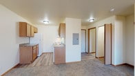 This single-floor unit offers a practical and comfortable layout across several well-defined areas. The open-concept living space is anchored by plush carpeted flooring and a ceiling fan, creating a relaxed and functional atmosphere. A sliding glass door leads to a private balcony, filling the room with natural light and providing pleasant outdoor views of the surrounding area.

The kitchen is efficiently designed with warm oak cabinetry, laminate countertops, and durable vinyl plank flooring. It is fully equipped with white appliances including a refrigerator, electric range, microwave, and dishwasher, along with ample upper and lower cabinet storage. An electrical panel is conveniently located at the transition between the kitchen and living areas.

The bedroom is generously sized, featuring soft carpeting, a standard window that brings in natural light, and access to a spacious walk-in closet with a hanging rod for organized storage. The bathroom is clean and straightforward, appointed with a tub-shower combination, toilet, and a wall-mounted towel bar. Throughout the unit, warm wood-toned trim and neutral wall colors contribute to a cohesive and inviting aesthetic. The overall design prioritizes functionality while maintaining a comfortable living environment.